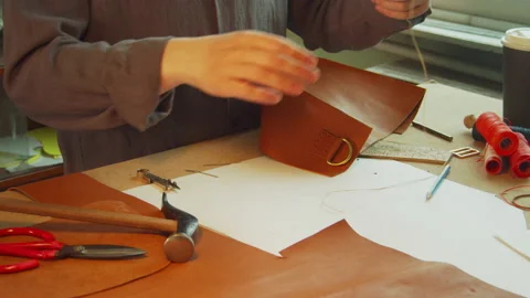 The master of exclusive leather goods unwinds and cuts the tailor's thread with Stock Footage 143720752
