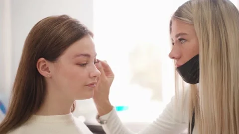 A master eyebrow artist models the eyebrows of a young woman in his office. 库存影片 144639593