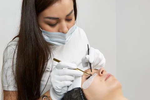 The master of eyelash extension uses tweezers to fix the eyelashes. Stock Photos