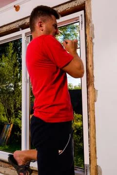 The master fixes a window to a wall by means of a manual key, installation of a Fotos de archivo