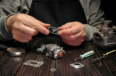 A master is focused on assembling parts of a small engine on a wooden table.  Stock Photos