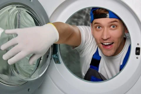Master happily opens round glass door washing machine from inside with his hand Stock Photos