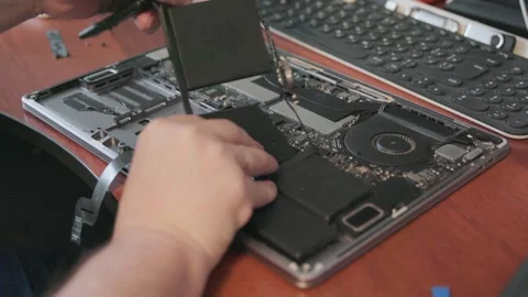 The master holds a disconnected battery with a cable over the opened laptop case Stock Footage 337828419