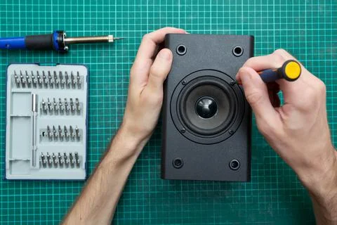 Master holds a screwdriver while repairing an audio speaker. Workplace with a Stock Photos