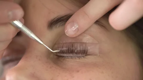 The master laminates the eyelashes of a young beautiful girl. 4K close-up Video stock 296087955