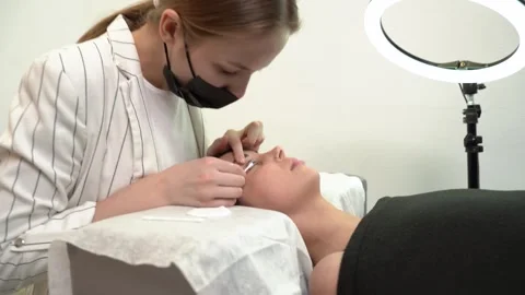 The master laminates the eyelashes of a young beautiful girl. 4K close-up Stock Footage 296087968