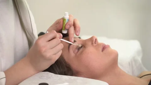 The master laminates the eyelashes of a young beautiful girl. 4K close-up Stock Footage 296087978