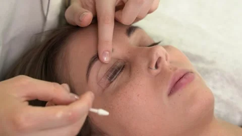 The master laminates the eyelashes of a young beautiful girl. 4K close-up Video stock 296088025