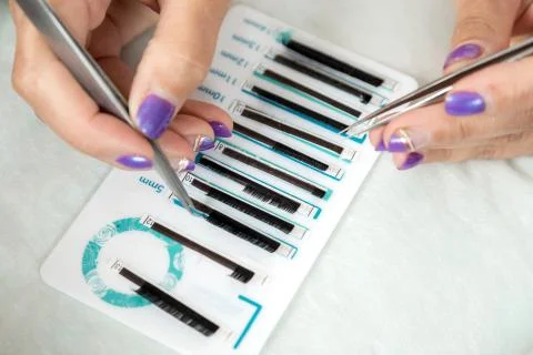 Master lash maker is holding one false eyelash by tweezers in hand Stock Photos