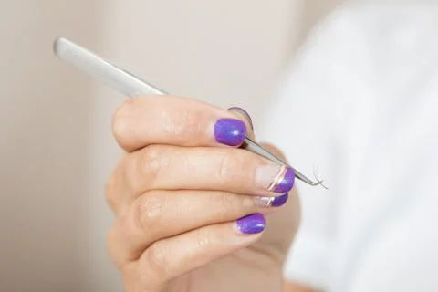 Master lash maker is holding one false eyelash by tweezers in hand Stock Photos
