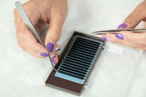 Master lash maker is holding one false eyelash by tweezers in hand Stock Photos