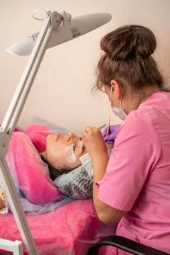 Master lashmaker, diligently extends eyelashes to the client, on the couch, in Stock Photos
