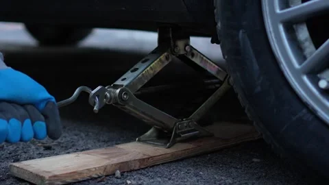 The master lifts a gray car on a mechanical jack for repair on the street. turns Stock Footage 320128103