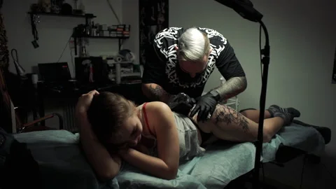 Master makes big tattoo on thigh and girl endures pain Stockbeeldmateriaal 104864214