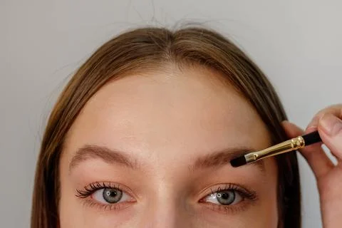 The master makes eyebrow coloring with a brush to a young beautiful girl in.. Fotos de archivo