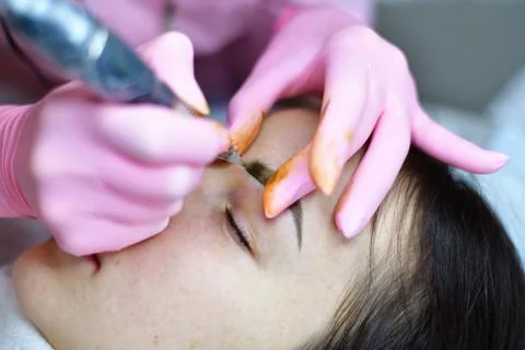 The master makes eyebrow tattoos for young girl. Stock Photos