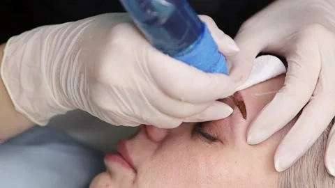 The master makes permanent eyebrow makeup with a needle tattoo machine Stock Footage 165115689