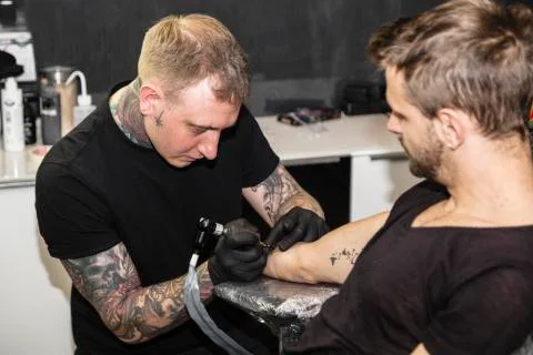 Master makes tattoo on arm of man in light studio Stock Photos