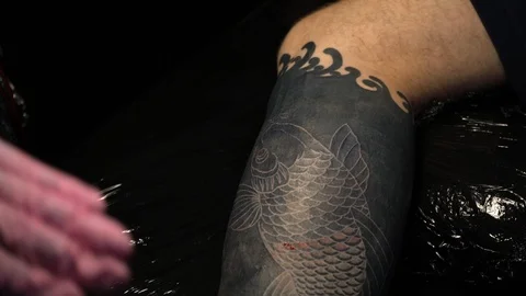 Master makes a tattoo on a leg. The artist with a beard in studio. Stock Footage