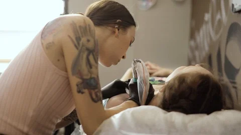 Master making tattoo for woman using tattooing machine in salon, side view. Stock Footage 113819565