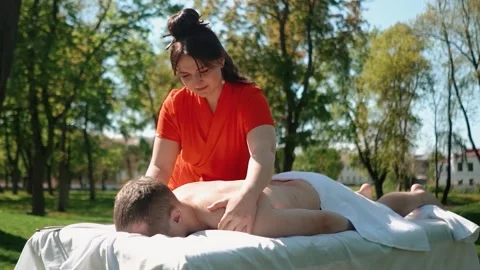 A master masseur in a bright orange uniform gives a healing body massage to a Stock Footage 274659450