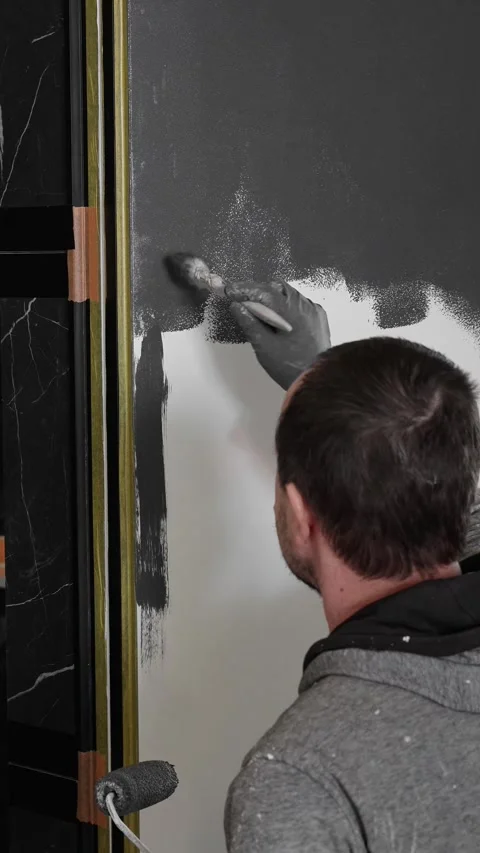 Master painter builder paints a concealed door in dark gray with a roller Stock Footage 317409515