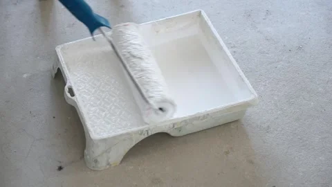 A master painter dips a roller into a paint tub filled with white paint Stock Footage 317901835