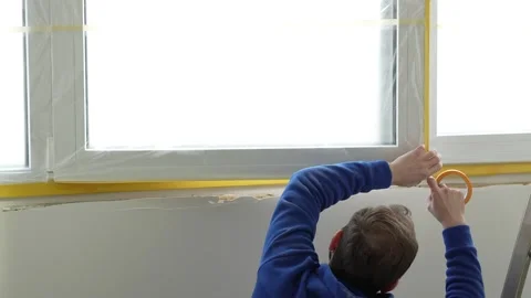 A master painter seals a window with protective film and tape. Stock Footage 317394829