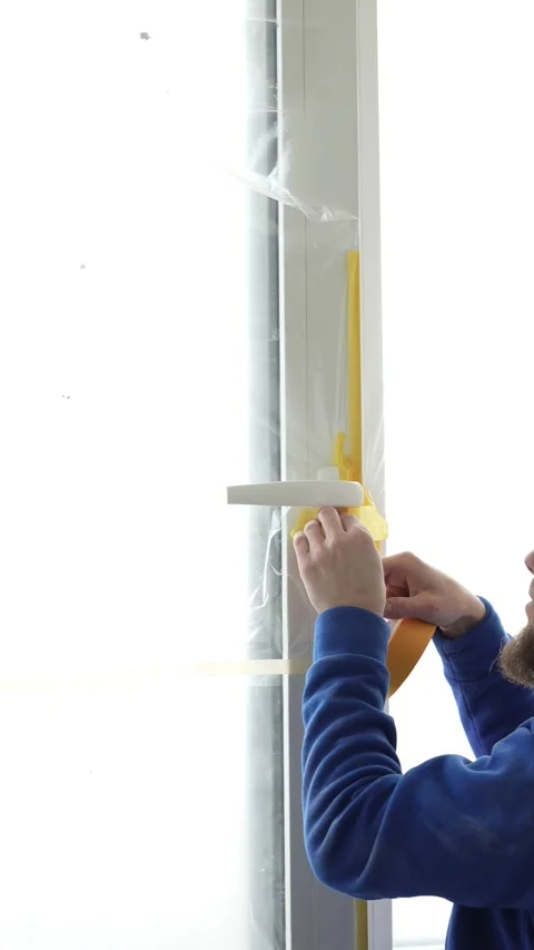 A master painter seals a window with protective film and tape. Video stock 317395193