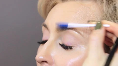 The master paints her eyebrows with an eyelash brush for a young woman in a beau Stock Footage 137571186