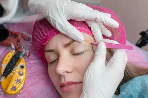 The master plucked the eyebrows of the client with thick brows in beauty salon Stock Photos