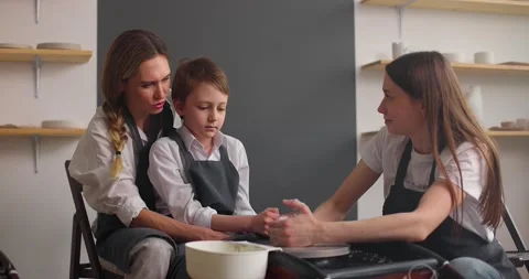 Master potter teaching mother with her kid in pottery workshop. Young female and Stock Footage 155649490