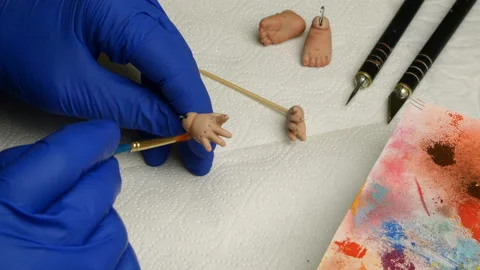 Master puppet intently paints fingers on dolls hand with thin brush. Stock Footage 128679023