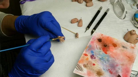 Master puppet intently paints fingers on dolls hand with thin brush. Stock Footage 128680236
