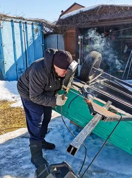 The master repairs a car trailer using electric arc welding. Stock Photos