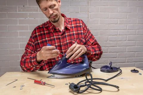 Master repairs the iron in the workshop on the table using tools 库存照片