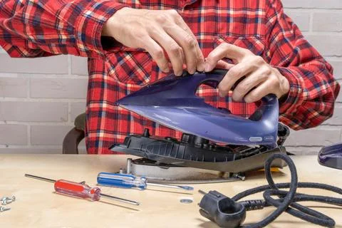 Master repairs the iron in the workshop on the table using tools Stock Photos