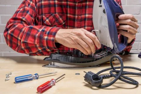 Master repairs the iron in the workshop on the table using tools Stock Photos