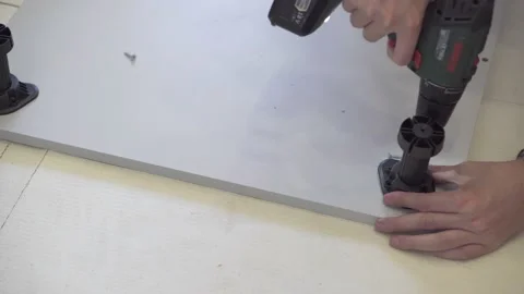 The master is screwing the plastic legs of the cabinet with a drill. Stock Footage 157288492