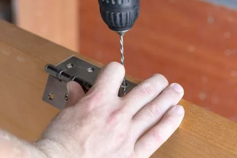 The master sets the door hinge. drills a hole with a tool Stock Photos