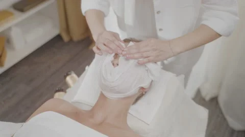 Master spa salon washes client face with warm towel with stroking movements. Stock Footage 197596814