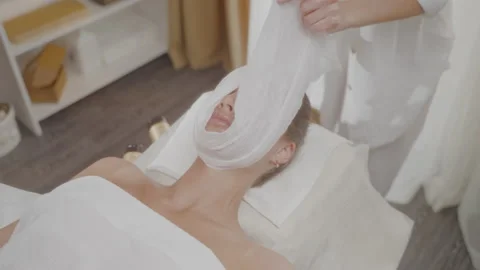 Master spa salon wraps warm towel around client face with massaging movements. Stock Footage 197596579