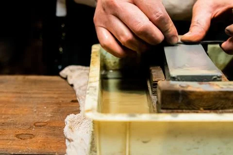Master swordsmith is sharpening knife on grindstone with water Stock-Fotos