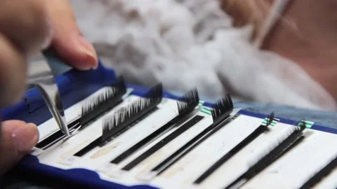 The master takes the eyelashes from the package for gluing to the patient with Vidéo 155156282