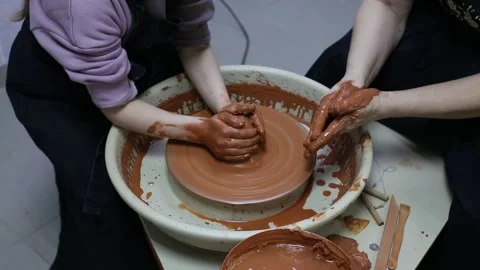 Master teaches apprentice how to make a clay pot on a potter's wheel Stock Footage 188716741