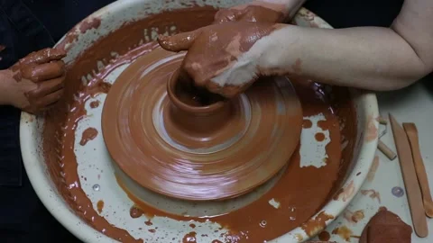 Master teaches apprentice how to make a clay pot on a potter's wheel Stock Footage 188741904