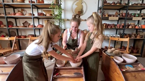 Master teaches two little girls to make a clay jug on a modern Potter's wheel Stock Footage 277789757