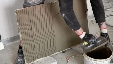 A master tiler applies adhesive to large-format tiles with a spatula Stock Footage 317901703