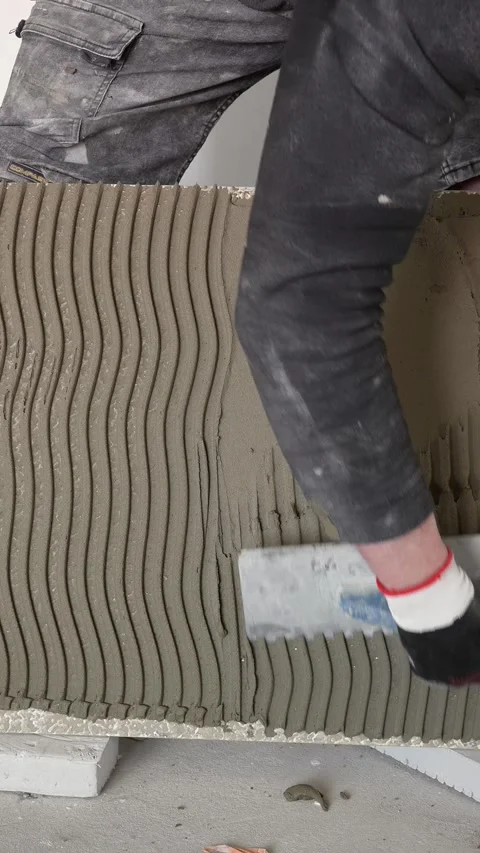 A master tiler applies adhesive to large-format tiles with a spatula Stock Footage 317902205