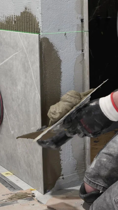Master tiler applies tile adhesive with a spatula to the wall Stock Footage 317902259